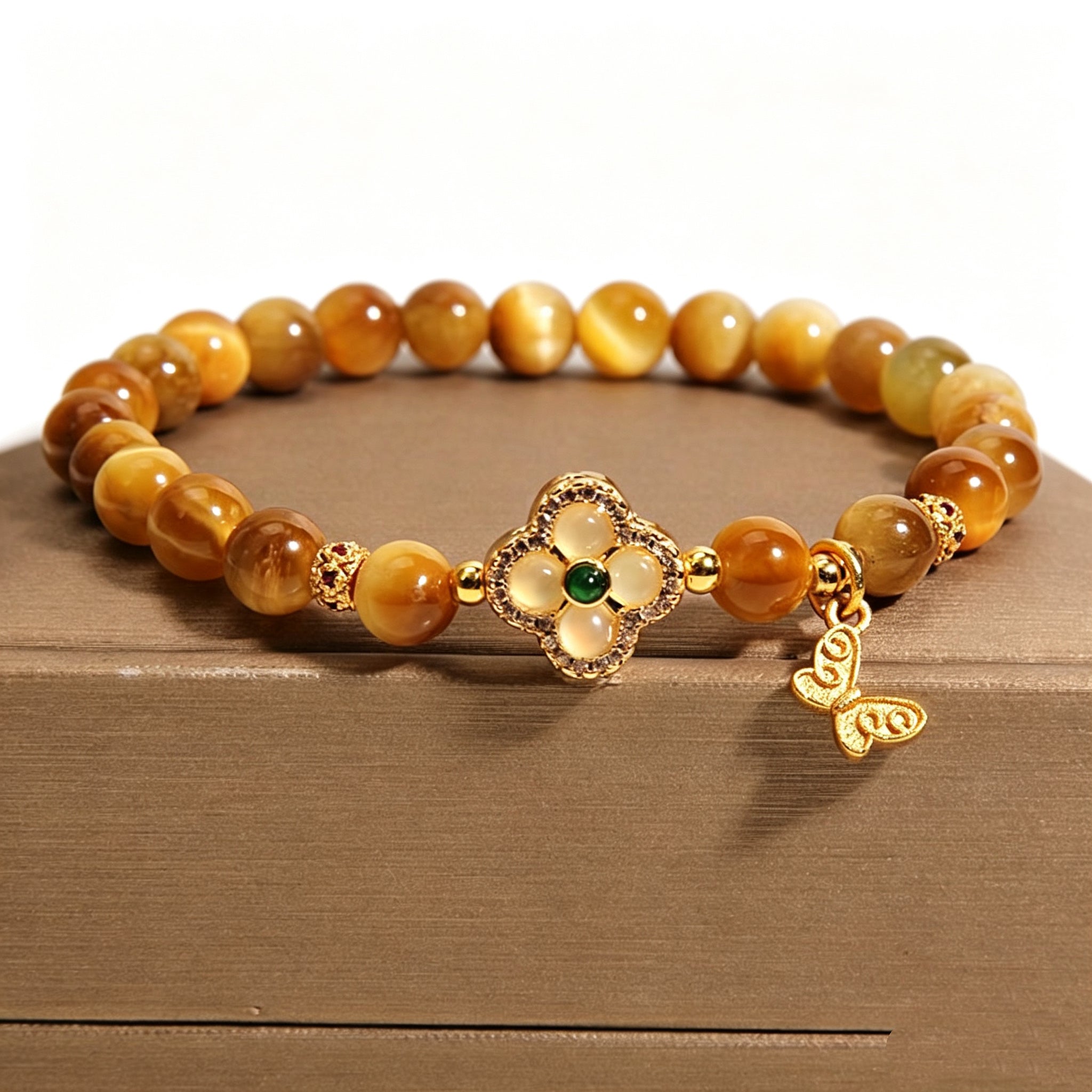 Macro close-up of four-leaf clover inlay ornament on Earthly Nurture golden tiger's eye bracelet, vintage oriental stone jewelry detail, solid white background