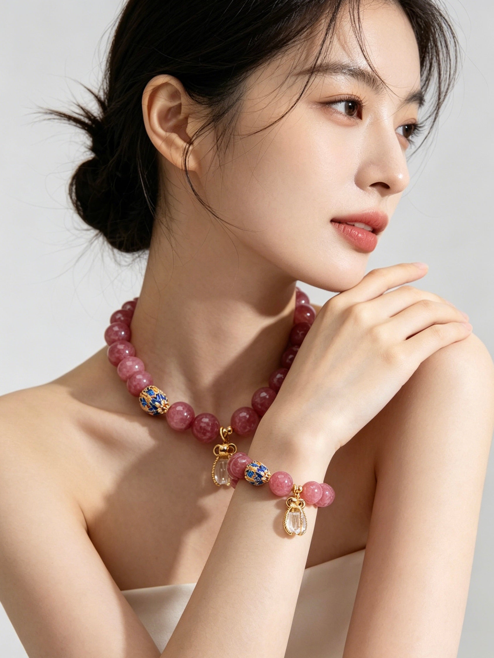 Women’s wrist close-up, fire series pink tourmaline bracelet with cloisonne enamel beads and clear quartz pendant, soft studio lighting